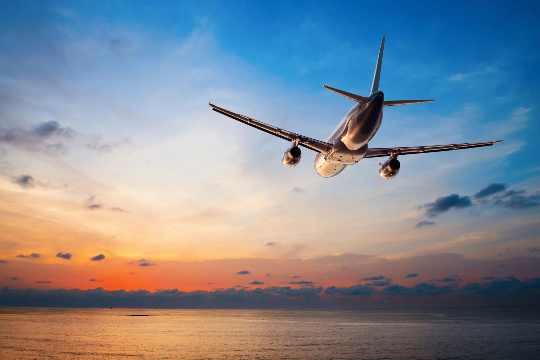 Airplane flying over the ocean at sunset.